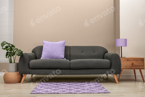 Preview: Stylish sofa with pillow, table and houseplant near beige wall indoors