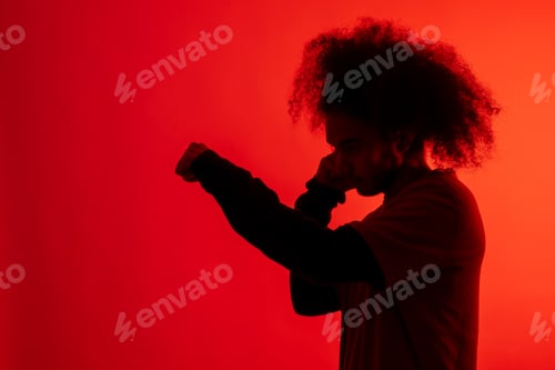 Preview: Silhouette with red light of boxer attacking. Young man with afro hair on white background