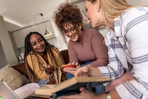 Preview: Diverse group female students learning at home using laptop and books for research.