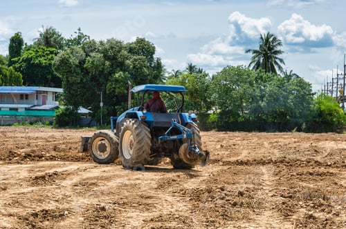 Preview: Farmer driving a blue tractor to plowing cultivated soil