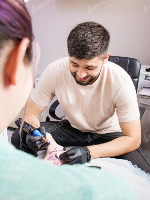 Preview: tattoo artist in black gloves working on a tattoo on the leg of a young woman tattooing a tattoo