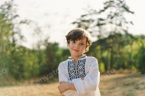 Preview: A boy smiles confidently while standing in a sunlit field, wearing a traditional embroidered shirt