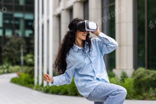 Preview: Young beautiful girl in shirt and jeans dancing outside office building wearing virtual reality
