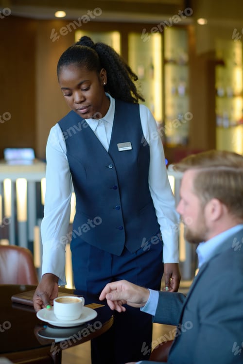 Preview: Young African American female manager of hotel bringing coffee to guest