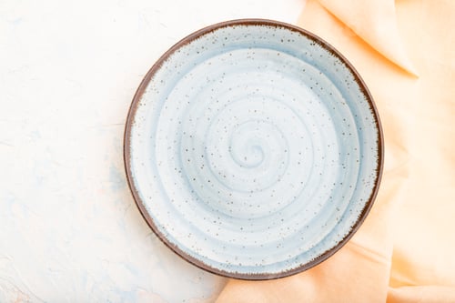 Preview: Empty blue ceramic plate on white concrete background. Top view.