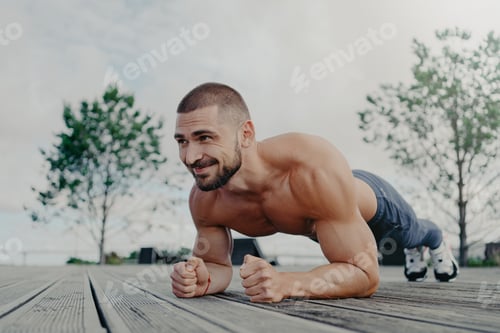 Preview: Shirtless determined bearded man with naked torso stands in plank pose and smiles gladfully