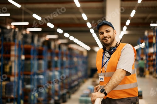 Preview: Happy warehouse worker at industrial storage compartment looking at camera.