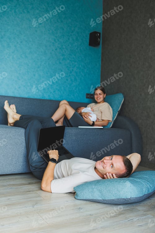 Preview: Parents with baby sitting on sofa at home with laptop and talking online. A young family