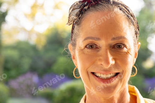 Preview: Smiling mature woman with headband and earrings enjoying outdoor garden setting, copy space