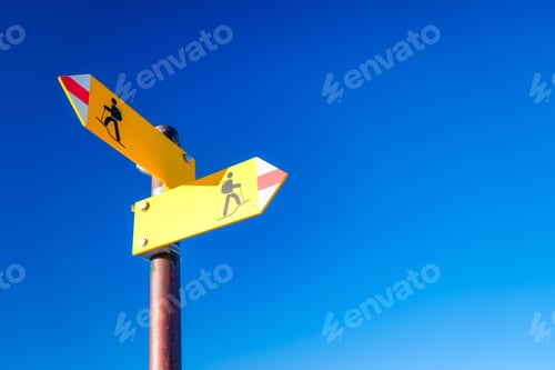 Preview: Directional marker for a mountain hike. Yellow bright sign with an arrow against the blue sky.