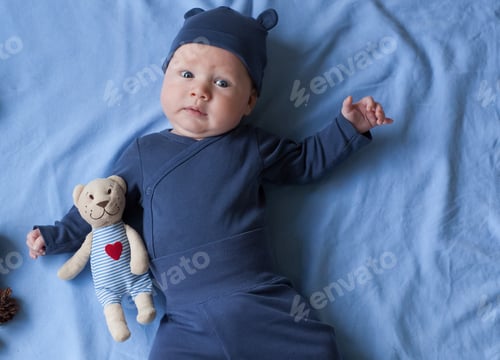 Preview: baby boy 3 months lies and smiles and holds a small toy bear in his hands.
