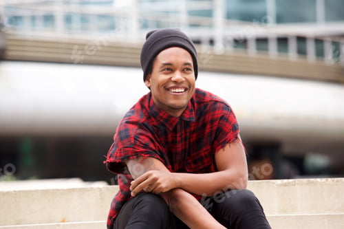 Preview: happy african american man sitting outside in city and smiling