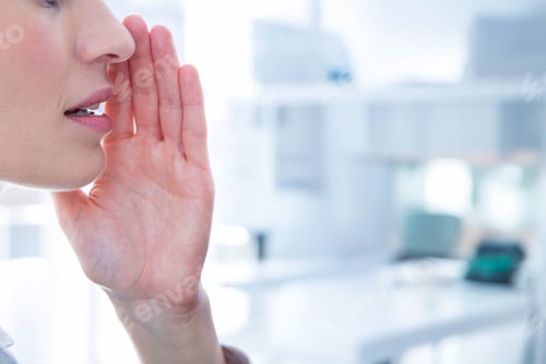Preview: Woman whispering softly into raised hand in bright office with desk, keyboard, monitor and chair
