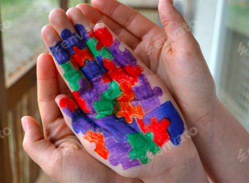 Preview: Mother holding hand of child with Autism puzzle pieces colored on palm of child's hand.