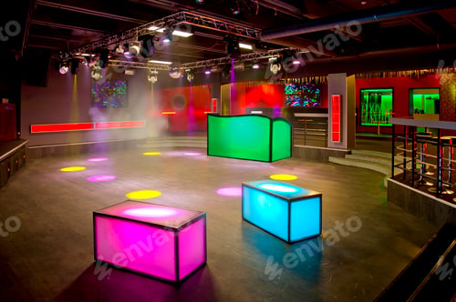 Preview: Nightclub interior, colourful lighting, wall screens and light boxes on a dance floor.