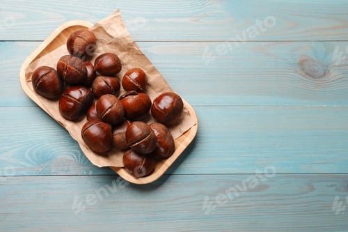 Preview: Fresh edible sweet chestnuts in serving plate on light blue wooden table, top view. Space for text