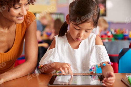 Preview: Elementary School Teacher And Female Pupil Drawing Using Digital Tablet In Classroom