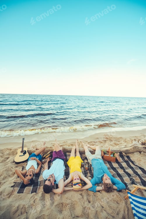 Preview: multiracial young people lying on blanket while spending time on sandy beach