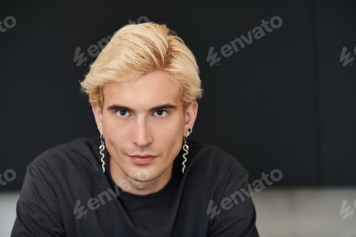 Preview: Young man with striking features and stylish earrings enjoys a moment in a modern apartment