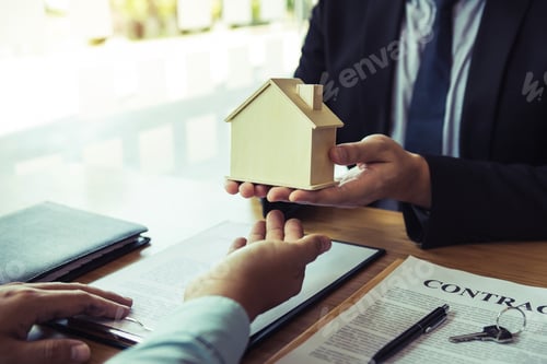Preview: Real estate agent congratulations to new buyer by giving house model to client in the agency office.