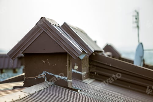 Preview: Close-up detail of new built brick plastered chimneys on house top with metal tile roof.