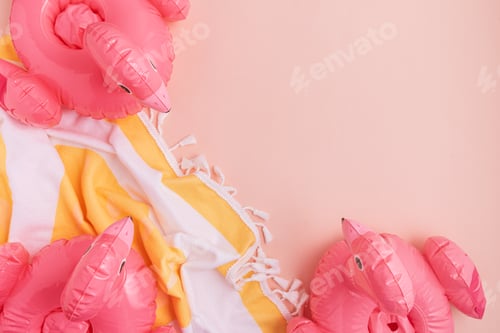 Preview: Beach essentials including an inflatable flamingos and towel on a light background.