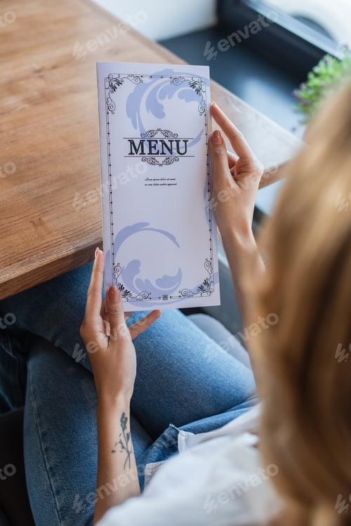 Preview: cropped view of blurred woman holding menu in restaurant