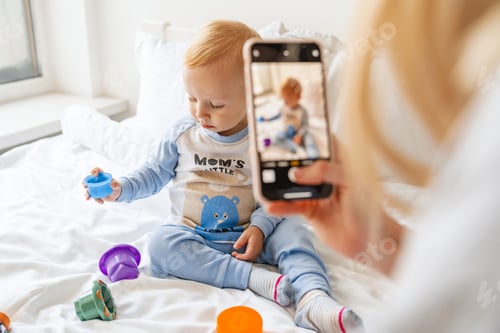 Preview: Mother taking photo of her blonde baby son on mobile phone