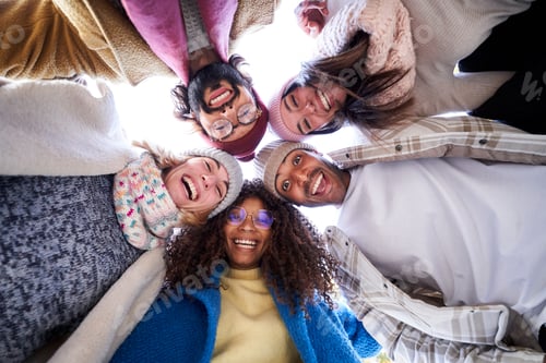 Preview: Multiracial group of happy friends doing a circle embracing, looking down to the camera cheerfully.