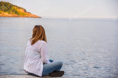 Preview: Woman sitting along shoreline in Tadoussac, Quebec at sunset