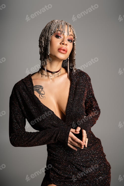 Preview: tattooed woman with sexy body posing in black lurex dress and jewelry wig isolated on grey