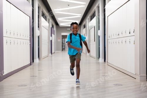 Preview: Full length of smiling african american elementary schoolboy running in corridor at school