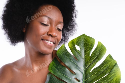 Preview: Close up shot of an african young girl shirtless holding tropical leaf isolated in white