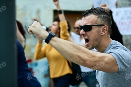 Preview: Angry Caucasian man with raised fist on a protest for human rights.