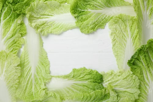 Preview: Frame with fresh ripe leaves of Chinese cabbage on white wooden table, flat lay. Space for text