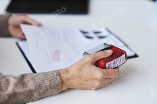 Preview: Focus on hand of mature female manager holding red rejected stamp