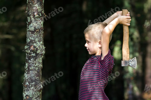 Preview: Small boy with heavy old iron axe cutting tree trump in forest on summer day.