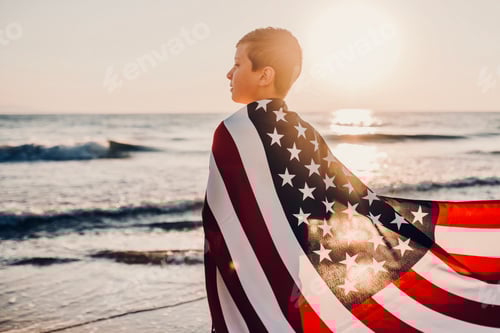 Preview: Back view Candid authentic gen Z boy wrapped American flag looks at the sea on celebrate July 4th