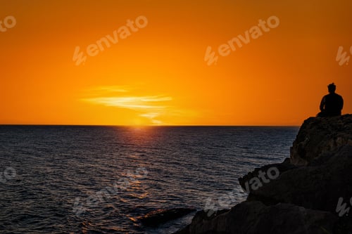 Preview: Silhouette of a person enjoying a peaceful evening, sitting on the beach looking at the sea