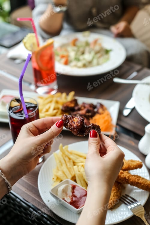 Preview: side view woman eats barbecue wings with french fries and ketchup with mayonnaise on a plate