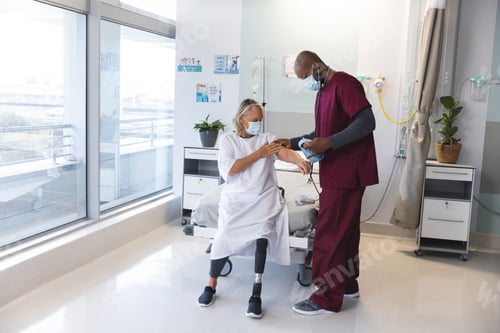 Preview: African american doctor measuring blood pressure of senior caucasian patient with prosthetic leg