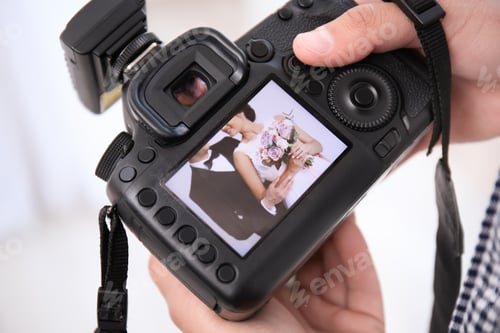 Preview: Professional photographer holding camera with lovely wedding couple on display, closeup