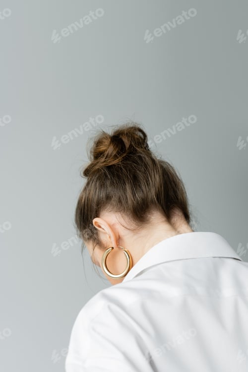 Preview: back view of young woman in golden hoop earring and white shirt isolated on grey