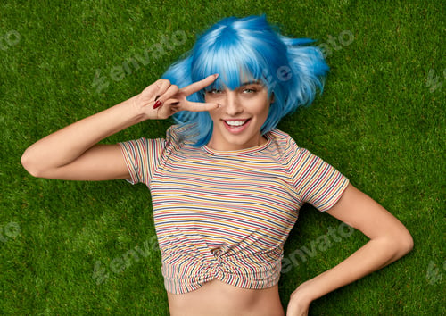 Preview: Woman with blue hair showing V sign on grass