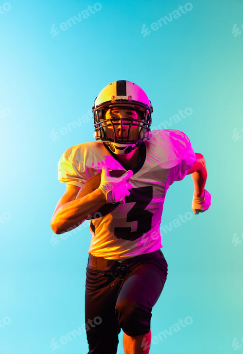 Preview: Close-up male American football player training isolated on blue studio background in neon light