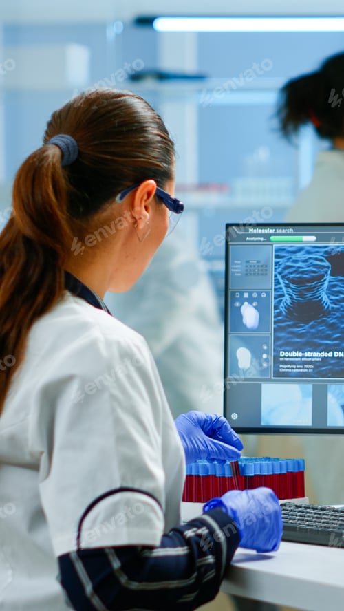 Preview: Laboratory doctor holding at blood sample and typing on computer