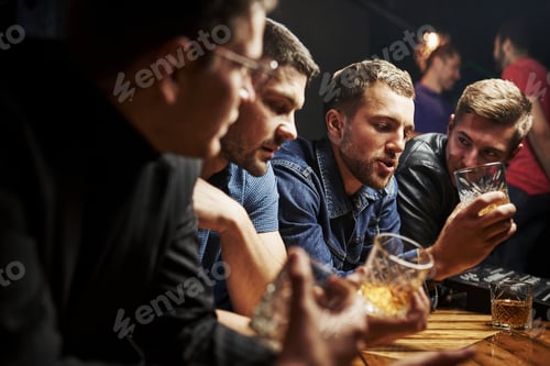 Preview: Side view. Friends resting in the pub with alcohol in hands. Having conversation