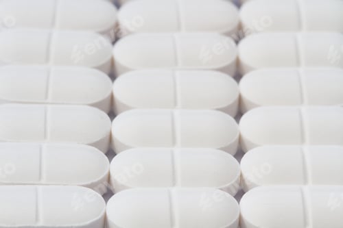 Preview: Rows of white pain relief tablets, pills, drugs and medicines in or a drug production background.