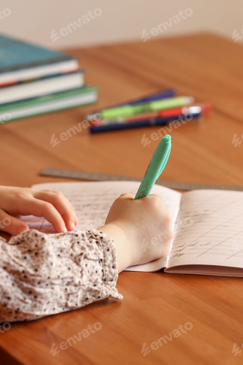 Preview: A cute girl sits at the table and writes letters in a notebook. Preparation for school