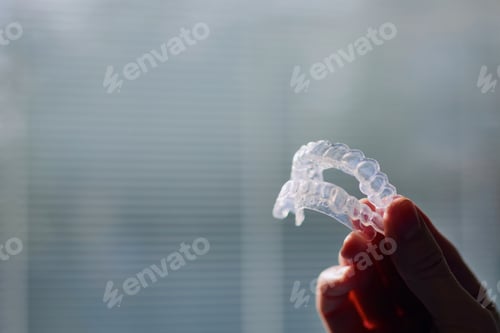 Preview: Close-up view of hand holding teeth whitening trays against window